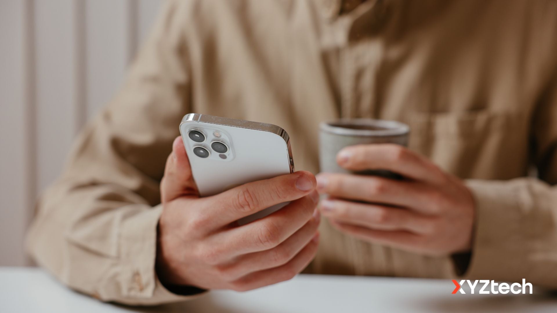 How to prolong iPhone battery life. A person holding an iPhone and a cup.